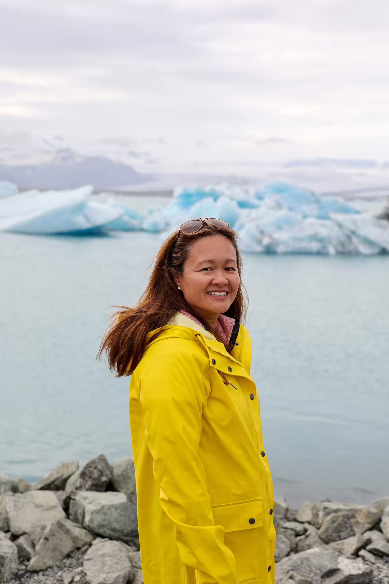 Smiling traveler in yellow jacket at Jokulsarlon Glacier Lagoon with blue icebergs on Iceland South Coast tour