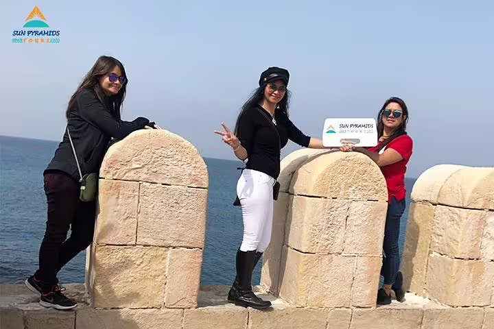Travelers at Alexandria Citadel seafront holding tour sign, add-on day trip from 5-day Cairo vacation package