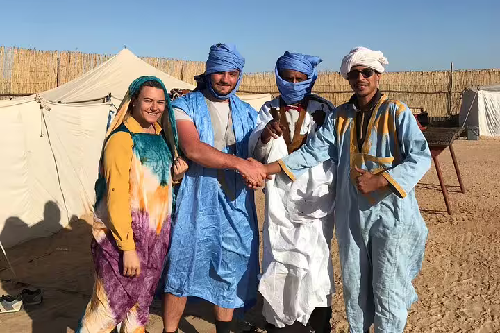Travelers in traditional Saharan robes at desert camp, cultural photo stop on Marrakech 3-day Morocco tour