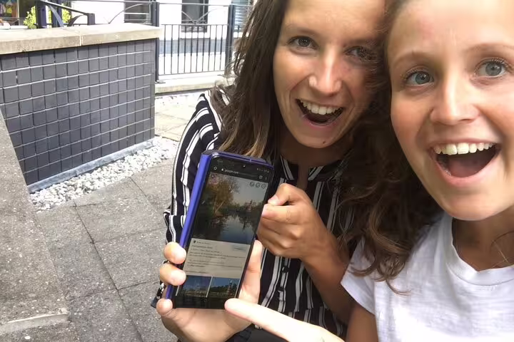Smiling travelers showing smartphone clues for a self-guided Pisa e-scavenger hunt, interactive walking tour app