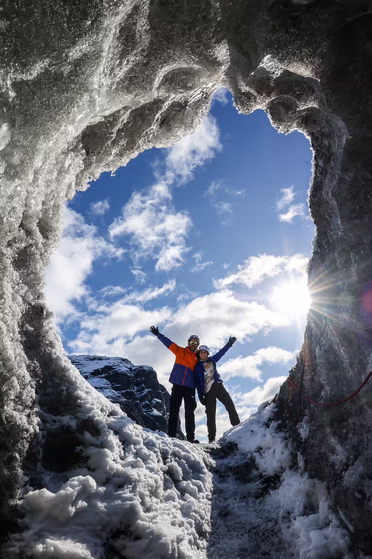 Two excited travelers posing inside a stunning ice cave opening on Vatnajokull Glacier Iceland tour