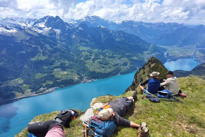 Trekkers resting on alpine summit above turquoise Swiss lake, scenic stop on 4-day Swiss Alps trekking tour
