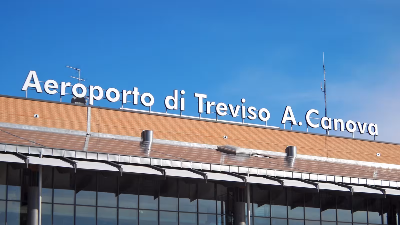 Exterior view of Treviso Airport featuring clear signage under a bright blue sky.
