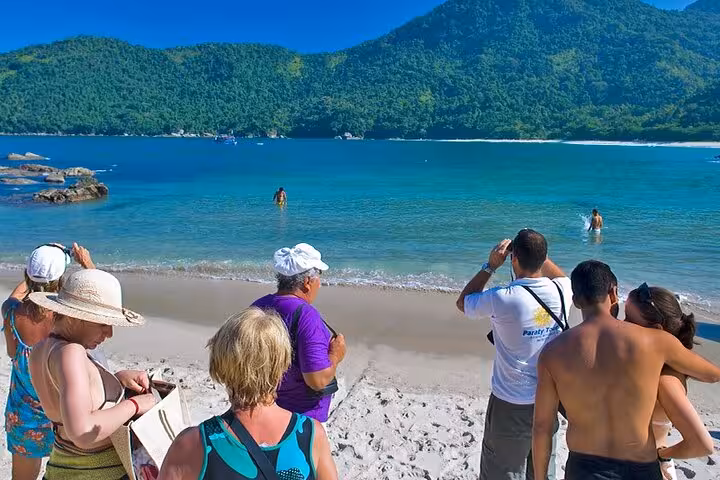 Tourists enjoying the sun and sea at a pristine beach in Trinidad, surrounded by lush green mountains.