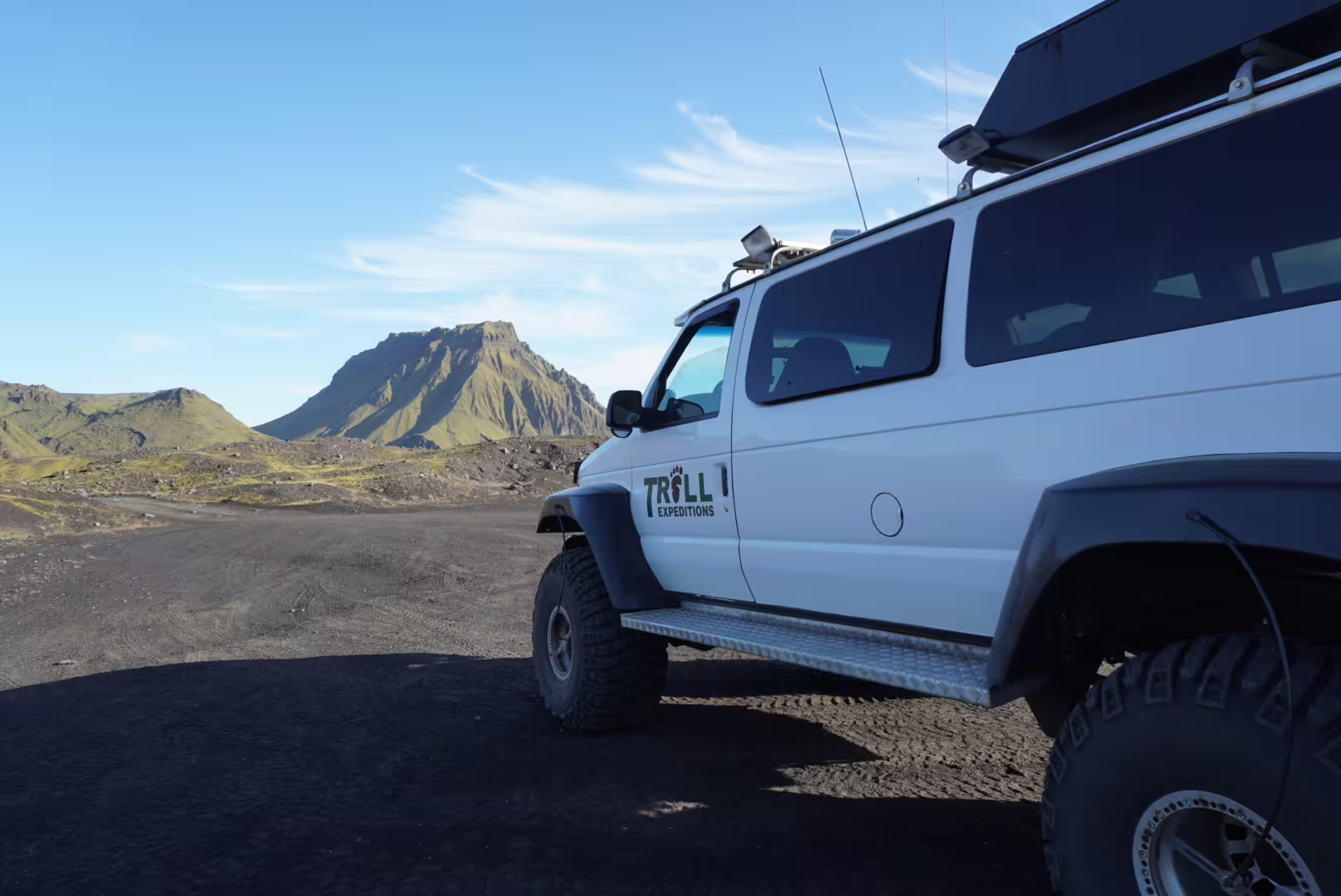 Troll Expeditions super jeep parked on black volcanic terrain with green mountains near Vik, Iceland