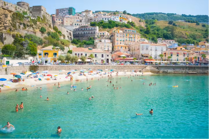 Spiaggia di Tropea affollata con mare cristallino, ombrelloni colorati e centro storico panoramico sulla Costa degli Dei