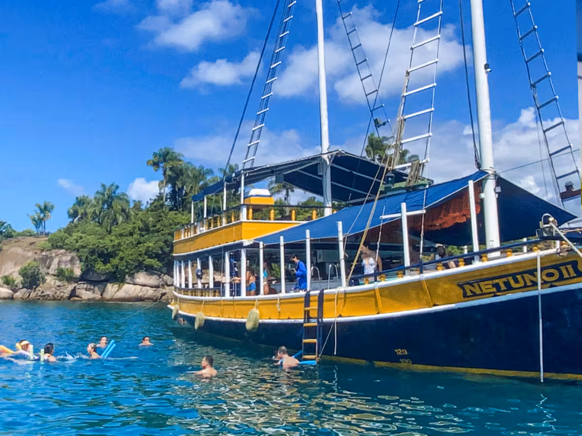 Tourists swim around a vibrant yellow boat enjoying a tropical five-hour caipirinha boat trip.