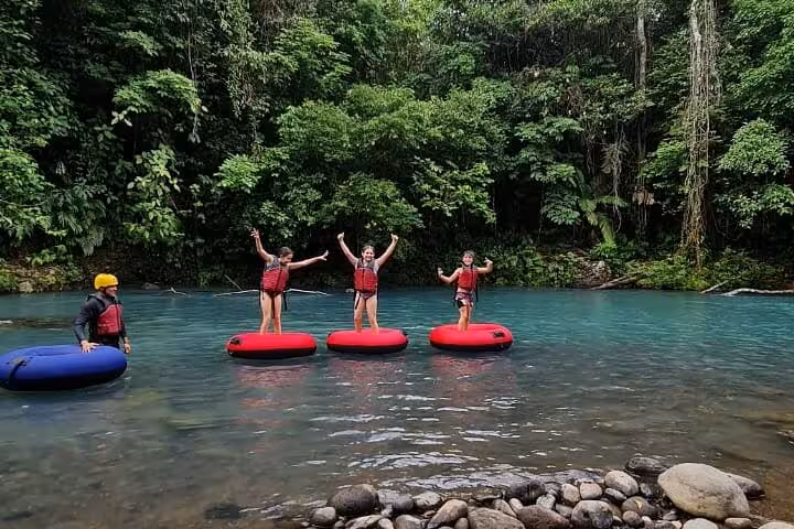 Adventurers tubing in Rio Celeste, surrounded by lush rainforest, enjoying an exciting nature and adventure tour.