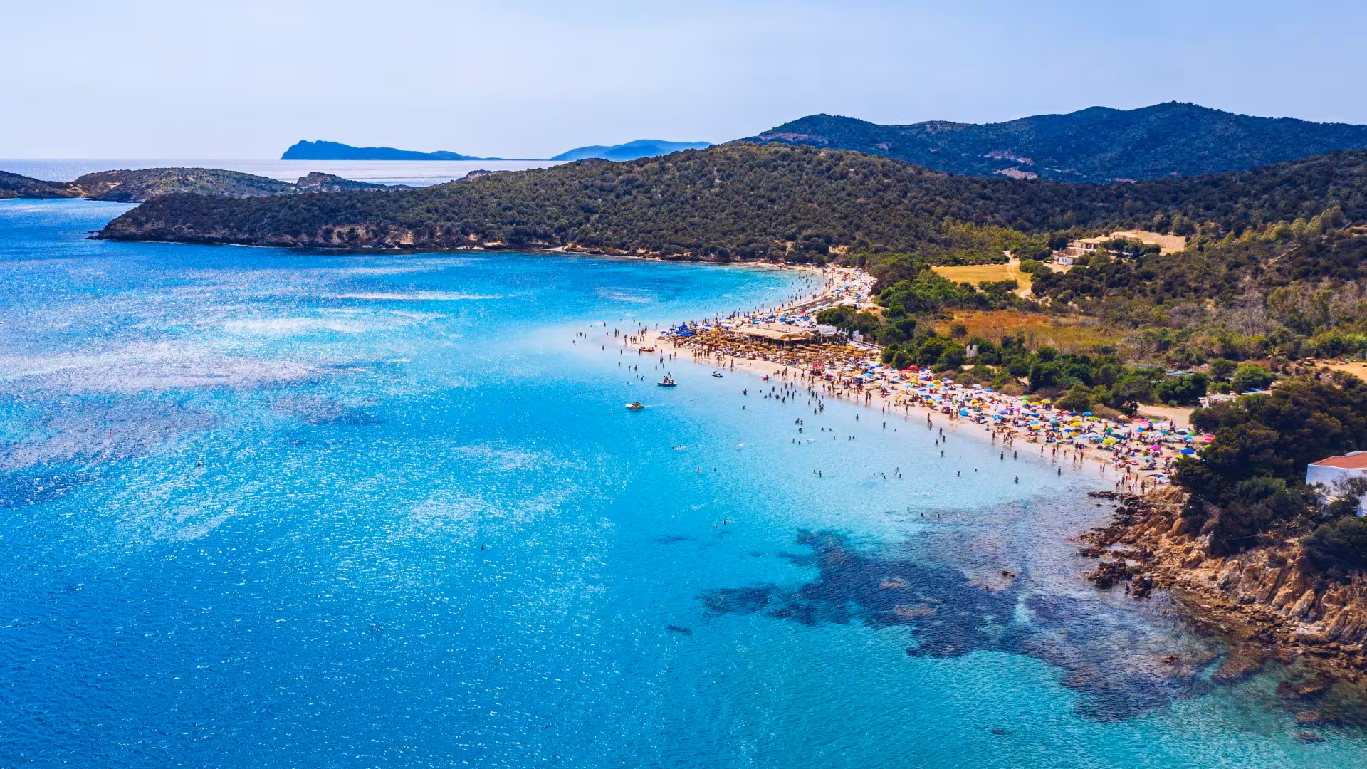 Vibrant Tueredda Beach with colorful umbrellas and crystal-clear waters, ideal destination on a Cagliari tour.