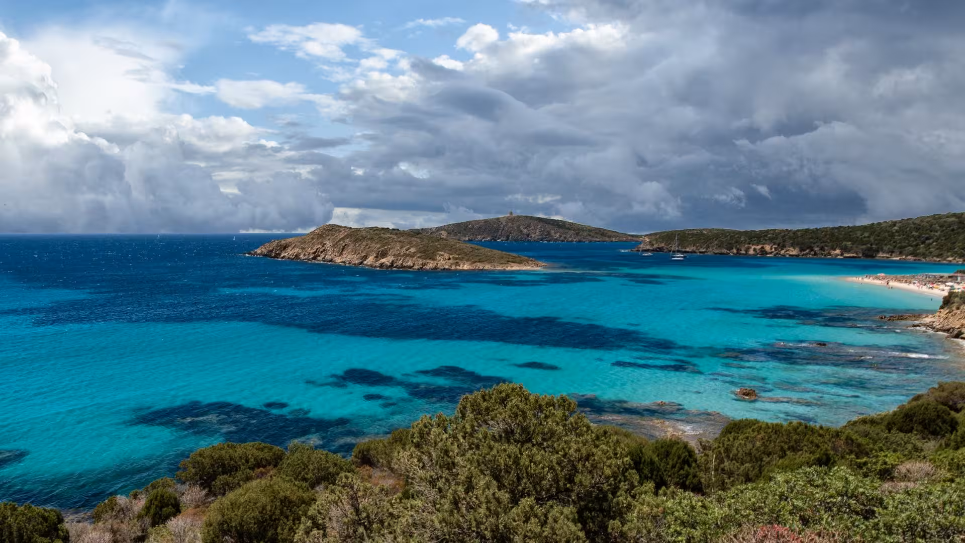 Breathtaking view of Tuerredda Beach's turquoise waters and lush islands under a dramatic cloudy sky near Cagliari.