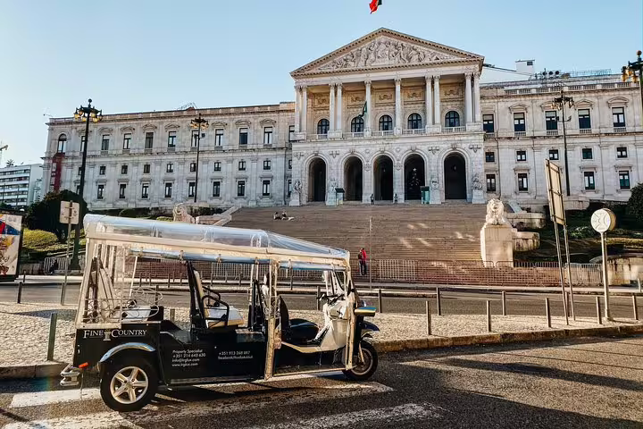 A tuk tuk parked in front of Lisbon's grand Sao Bento Palace, ready to explore Chiado and Bairro Alto on a vibrant tour.