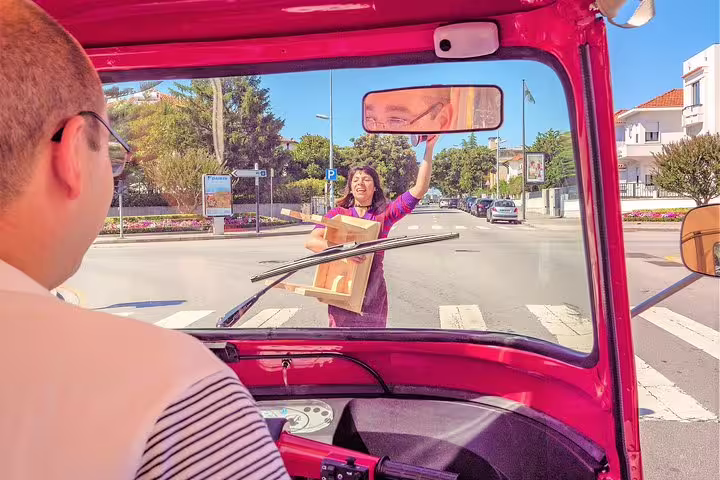 View from a tuk tuk in Porto showing a lively street scene with a person crossing a crosswalk on a sunny day.
