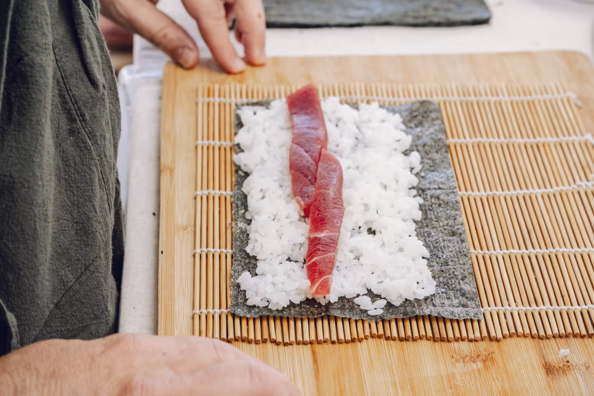 Close-up of tuna on sushi rice over nori sheet on bamboo mat, step-by-step maki rolling in sushi masterclass
