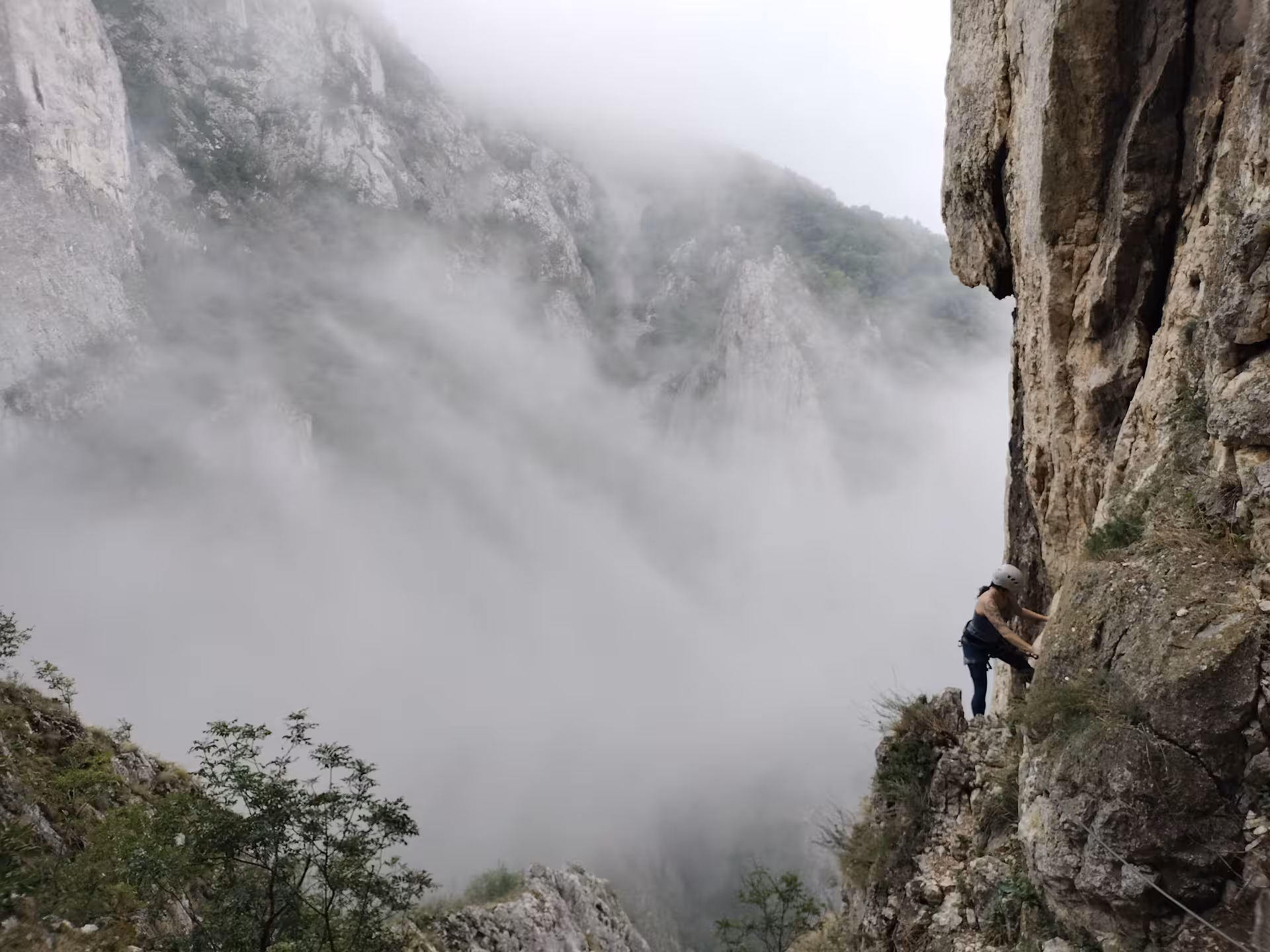 Climber scaling rocky cliff face above misty Turda Canyon with dramatic fog-filled gorge views