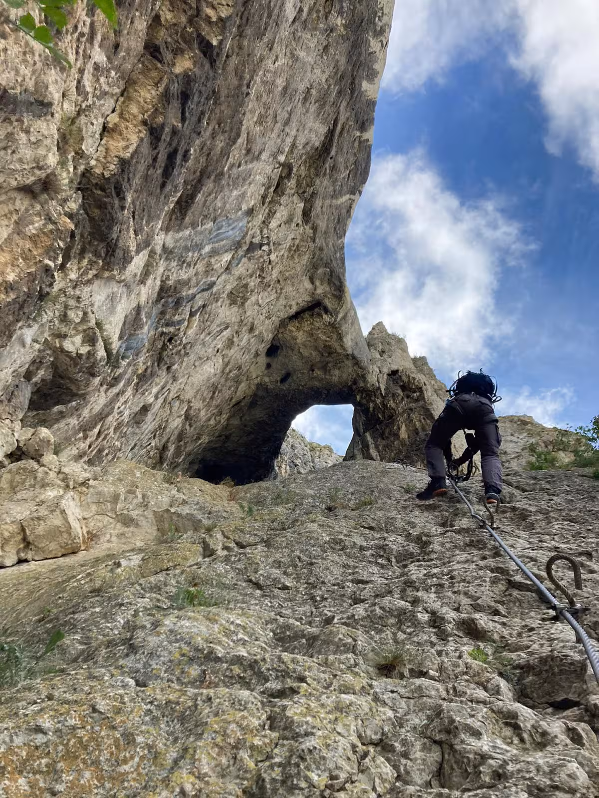 Climber ascending rocky cliff face with natural stone arch at Turda Canyon guided hiking tour