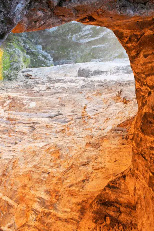Rock arch opening in Turda Canyon revealing layered sandstone walls and green valley beyond