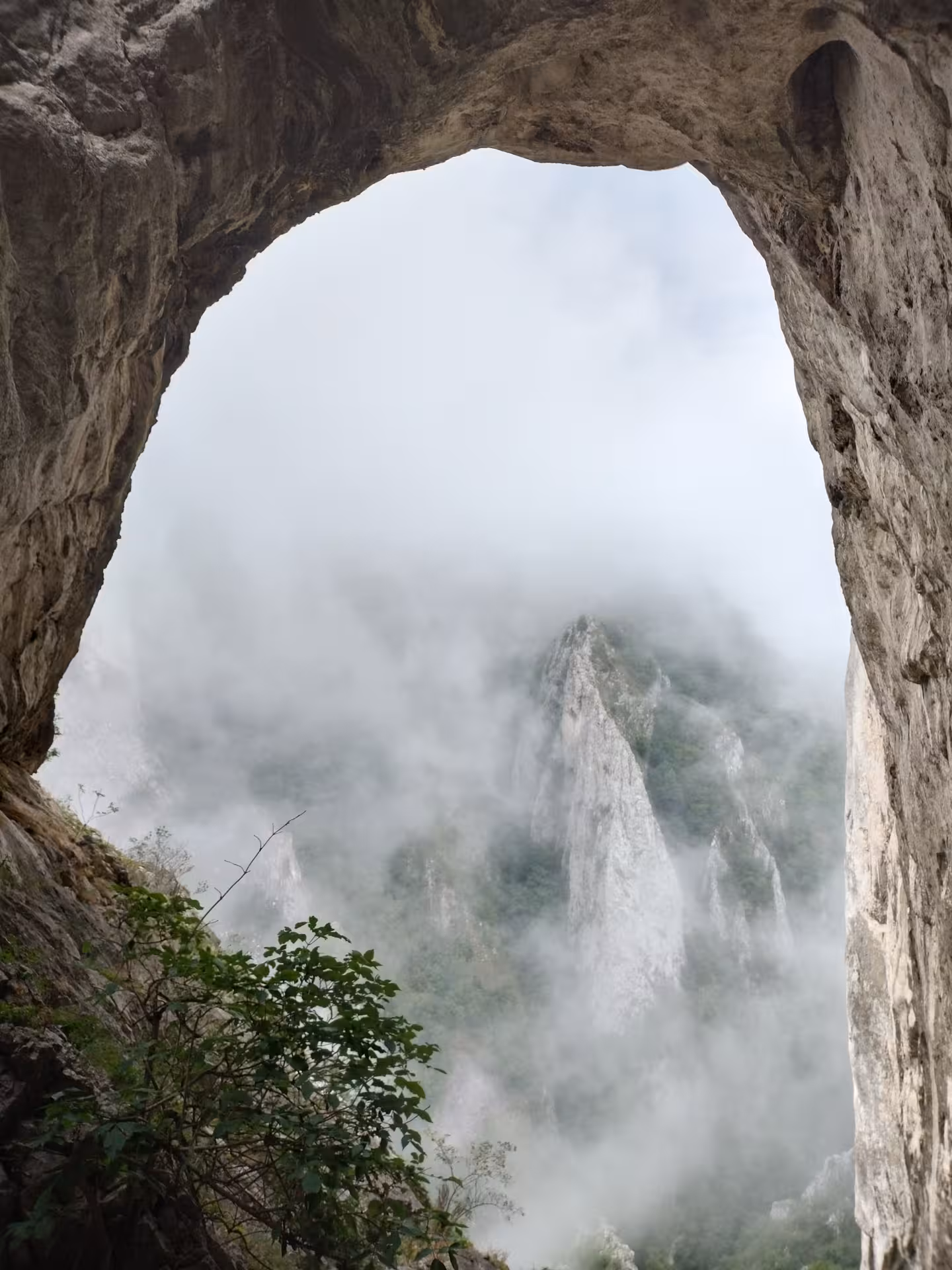Natural rock arch framing misty mountain peaks and limestone spires in Turda Canyon, Romania
