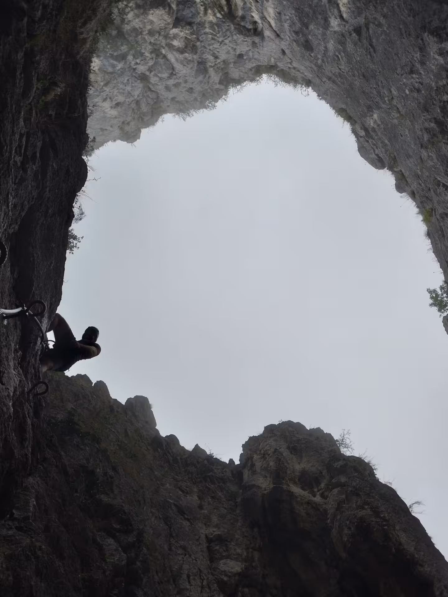 Rock climber ascending limestone cave wall in Turda Canyon viewed from below through natural arch opening