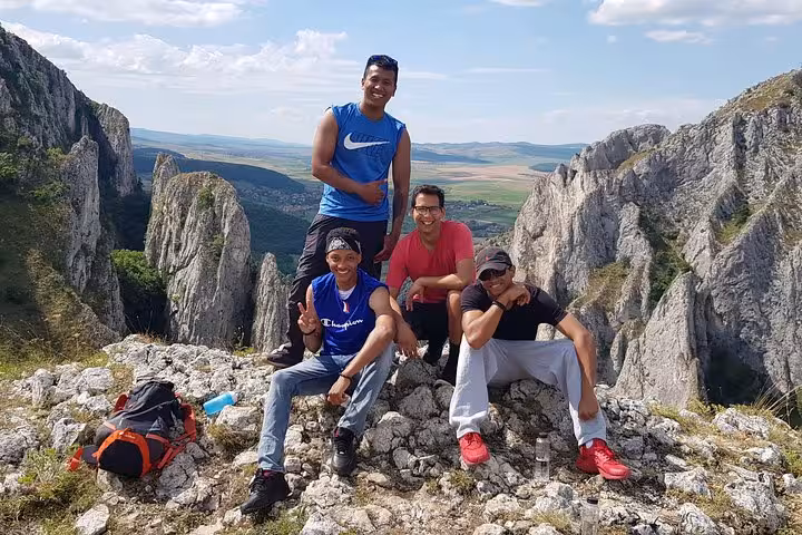 Four hikers posing on rocky summit at Turda Gorge with sweeping valley views behind them