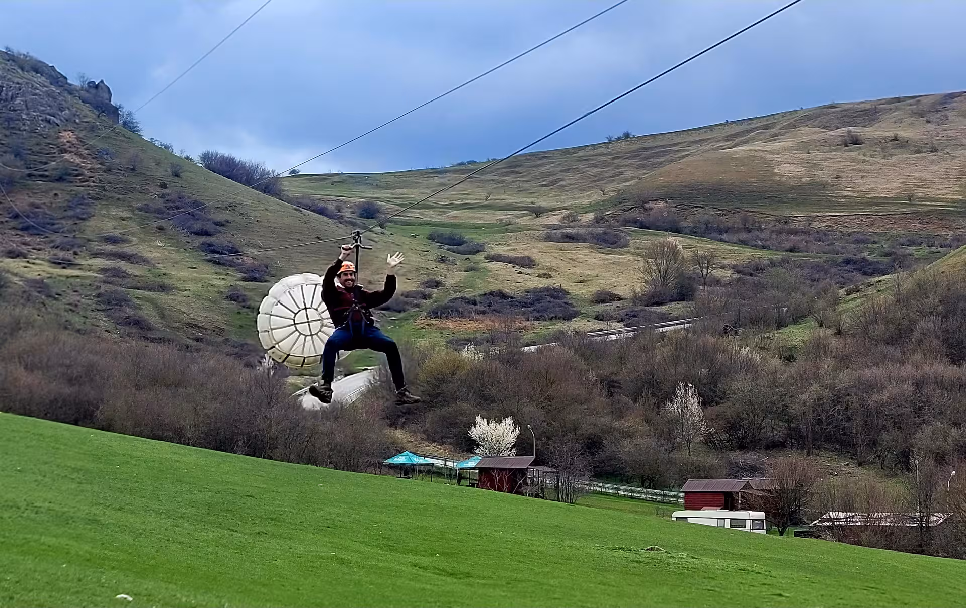 Man ziplining over green valley at Turda Gorge, waving and wearing safety helmet and harness