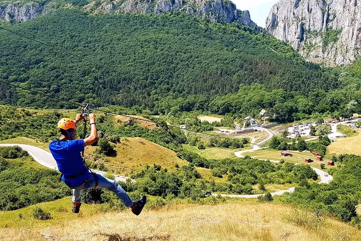 Person zip lining over Turda Gorge valley with lush green mountains and rocky cliffs in background