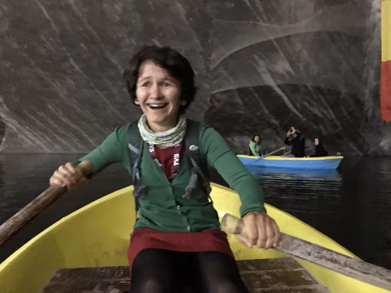 Woman rowing yellow boat inside Turda Salt Mine underground lake, smiling at camera