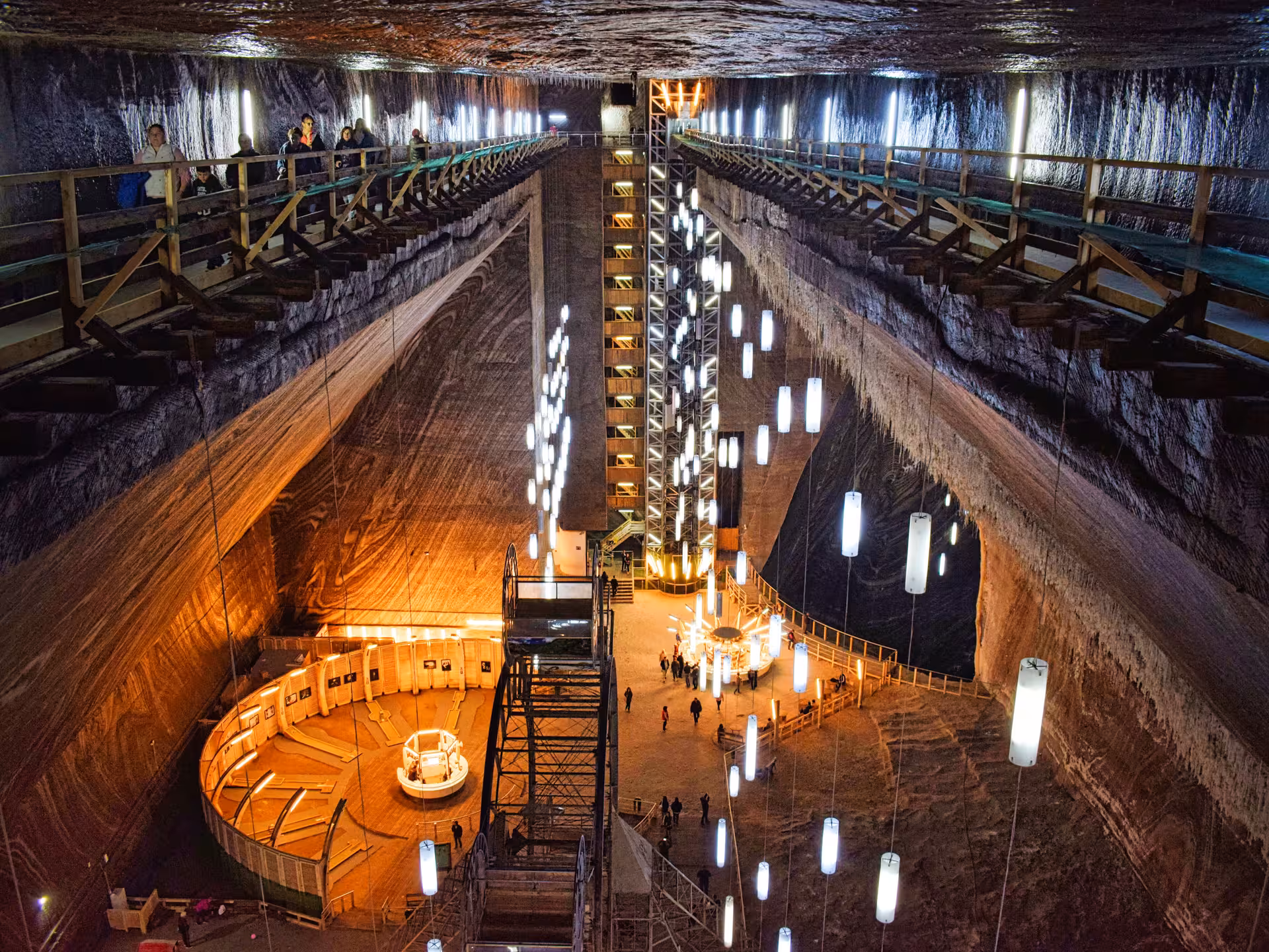 Breathtaking illuminated underground chamber inside Turda Salt Mine featuring glowing lights and tourists exploring