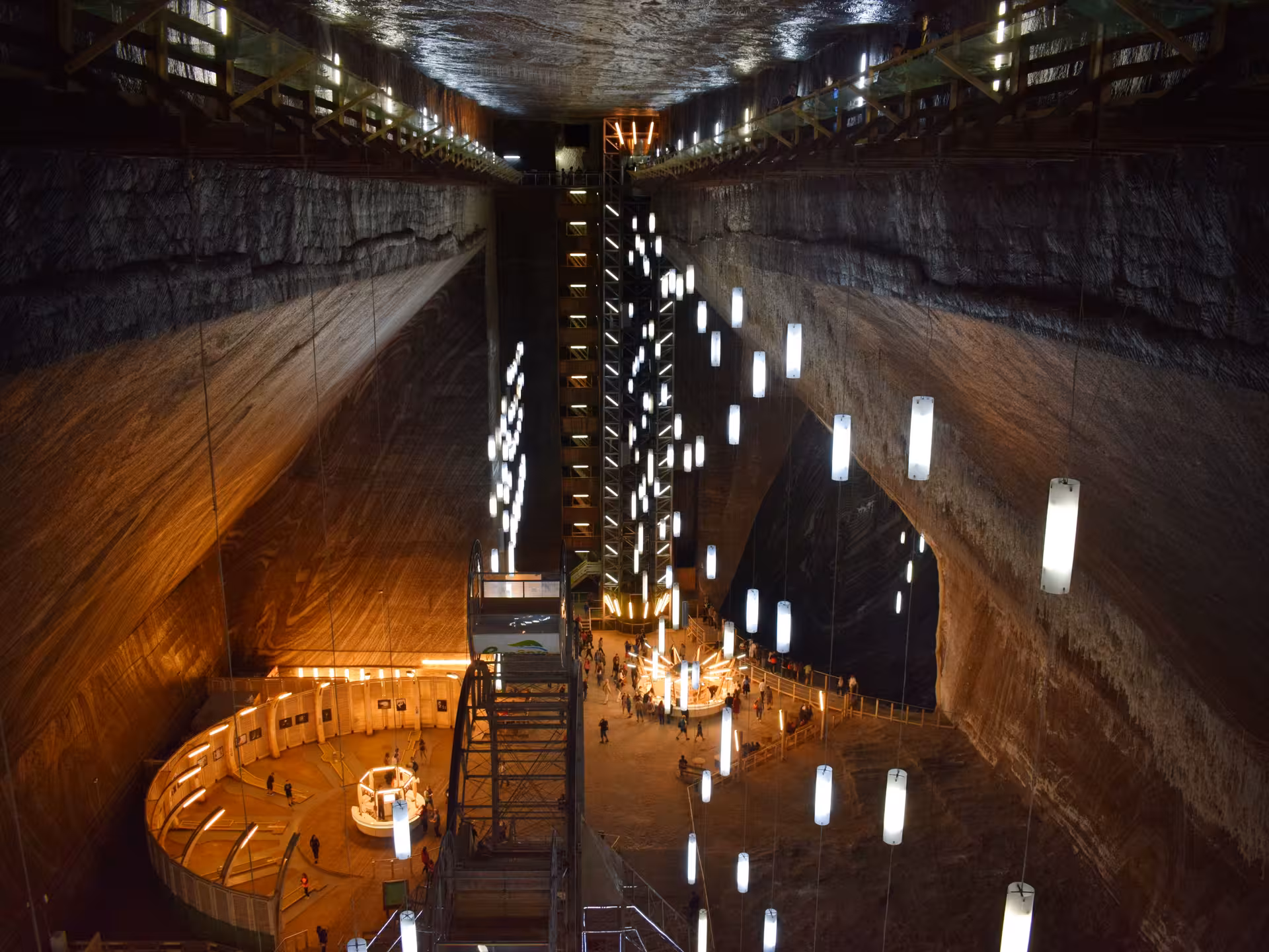 Stunning illuminated vast underground chamber of Turda Salt Mine with hanging lights and visitors exploring from Cluj guided tour