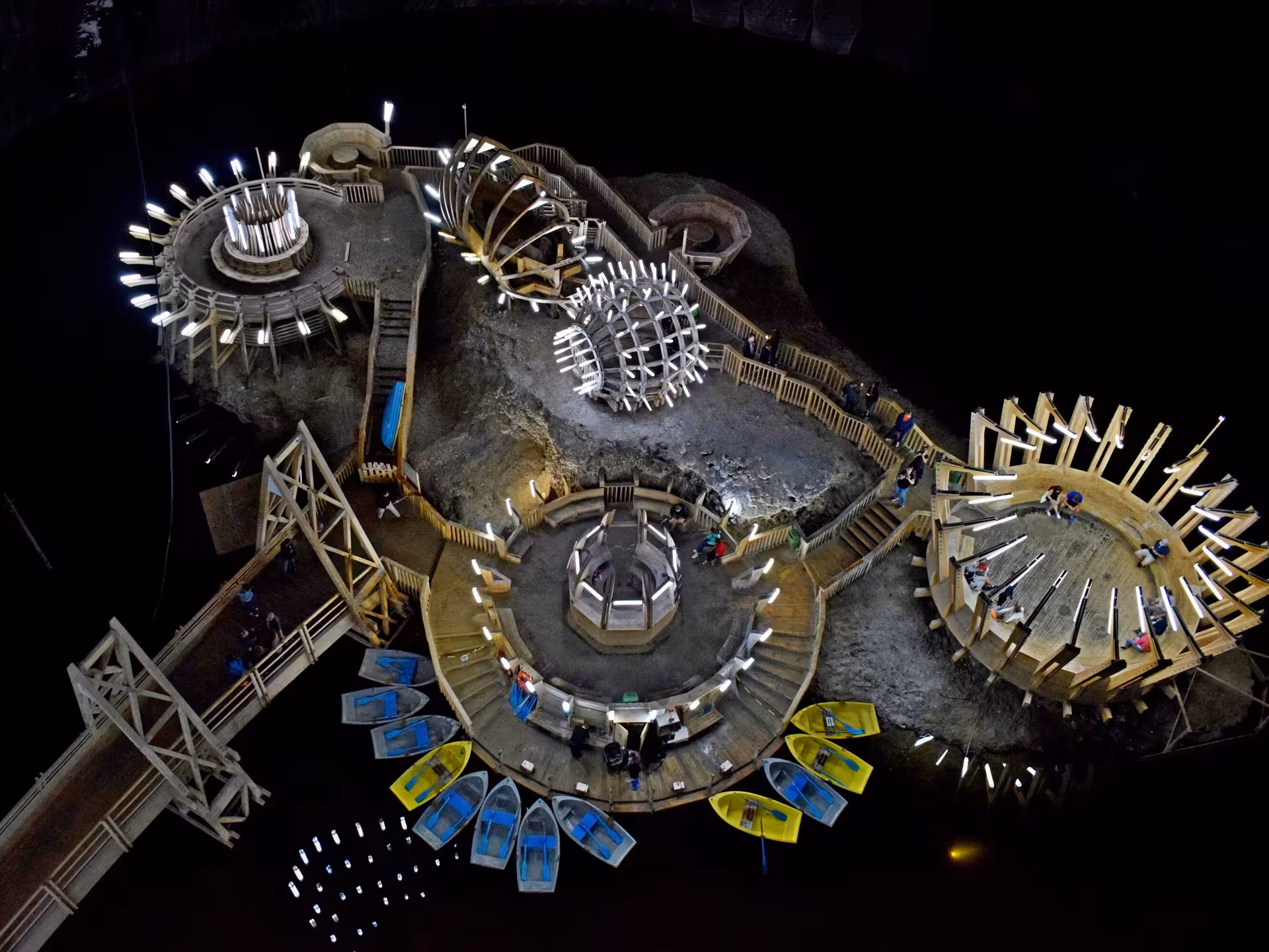 Aerial view of Turda Salt Mine underground island with wooden platforms, illuminated sculptures, and colorful rowing boats on dark saltwater lake