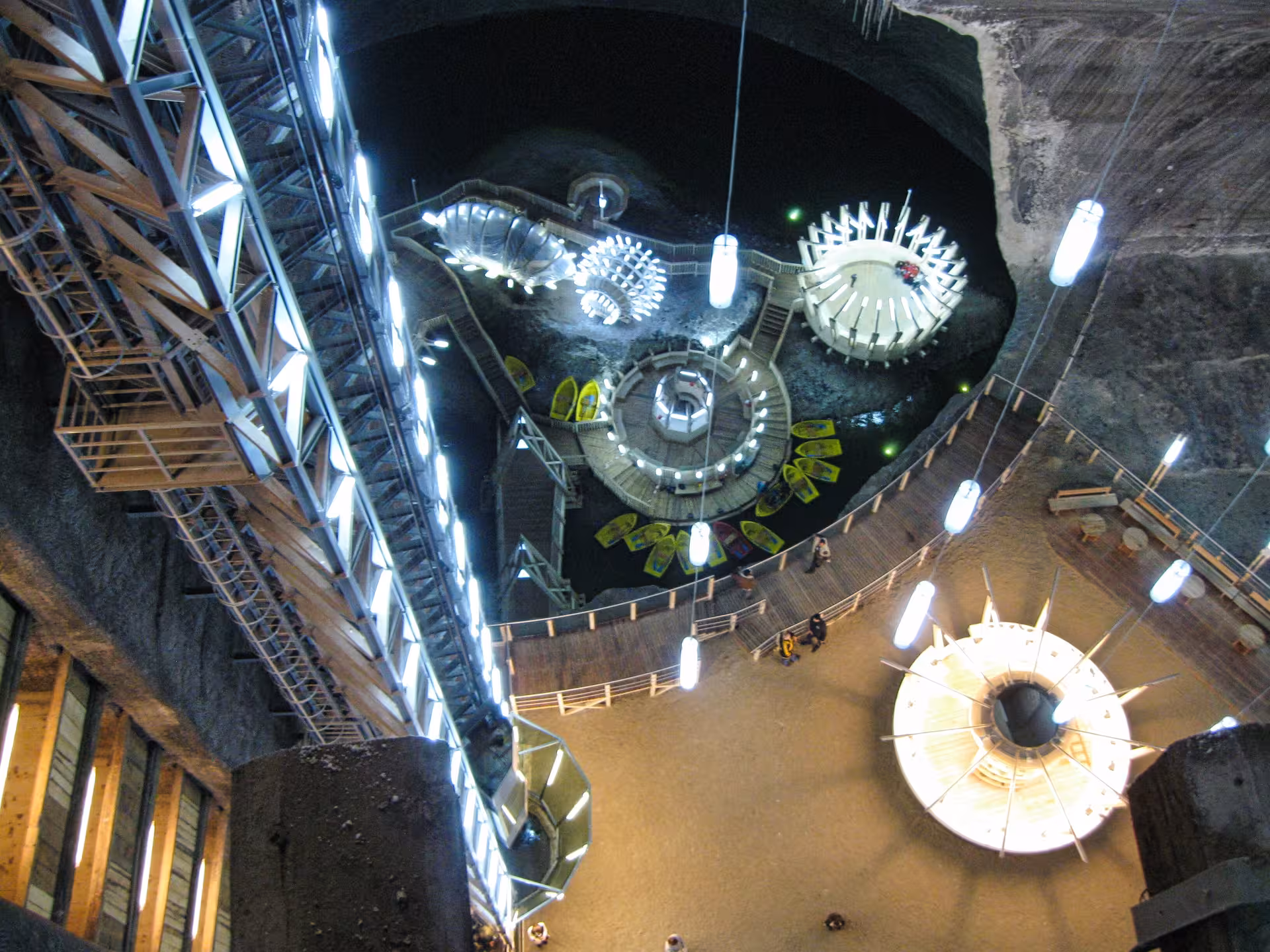 Aerial view of Turda Salt Mine underground chamber with boat lake, spiral staircase, and illuminated attractions