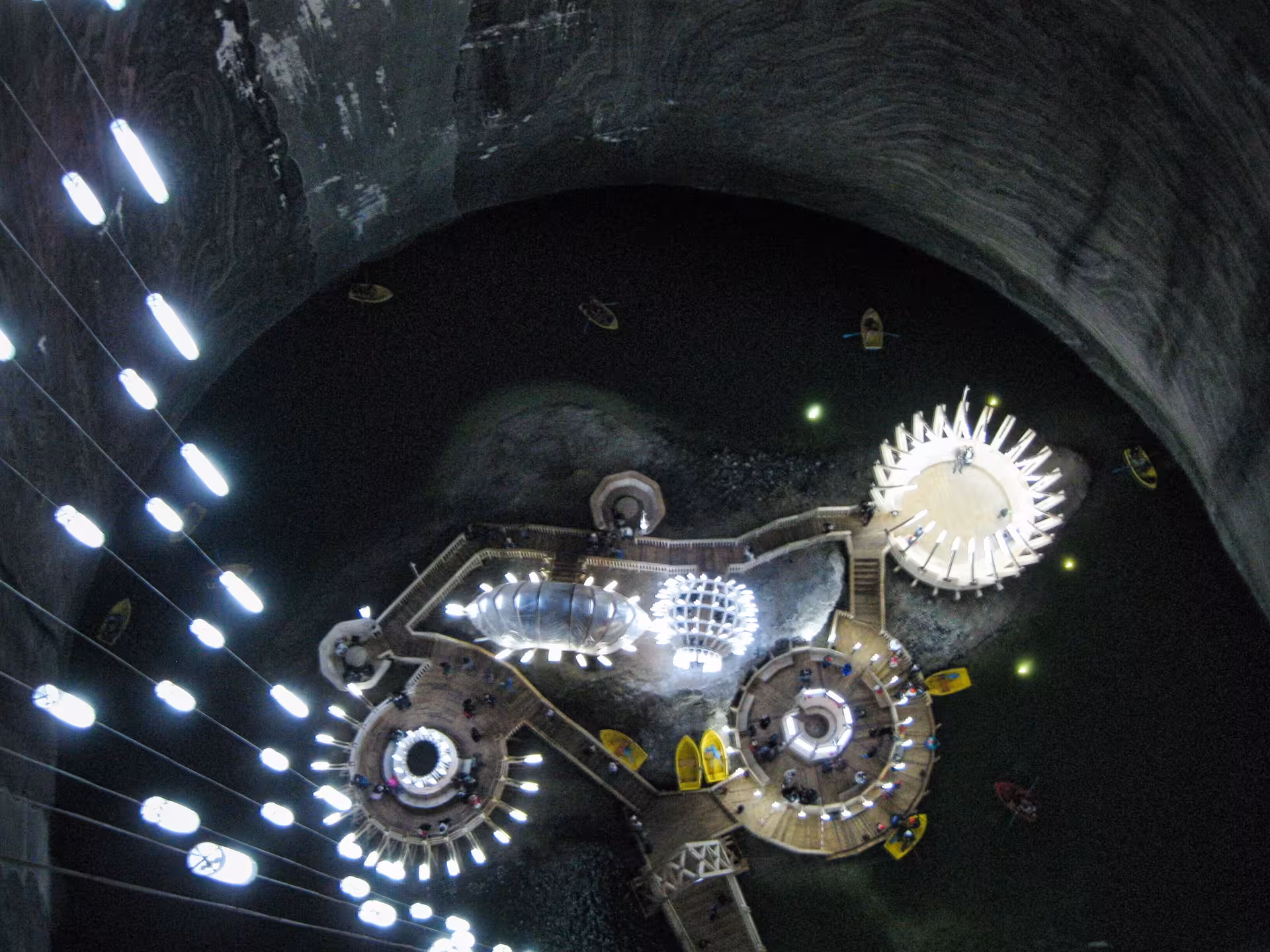 Aerial view of Turda Salt Mine underground cavern with illuminated platforms, Ferris wheel, and boats on subterranean lake