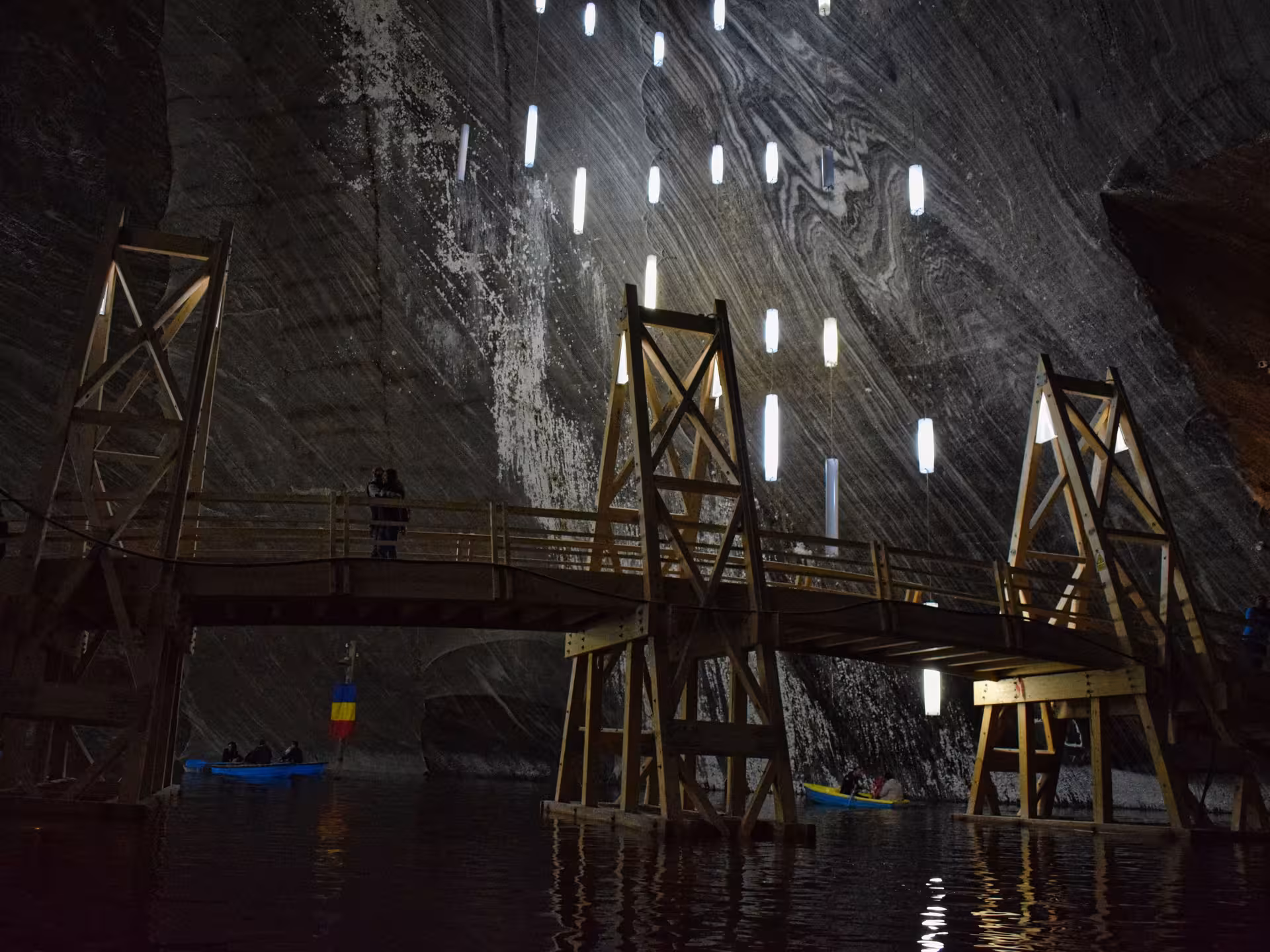 Underground boat ride on salt lake inside Turda Salt Mine with wooden bridge and hanging lights