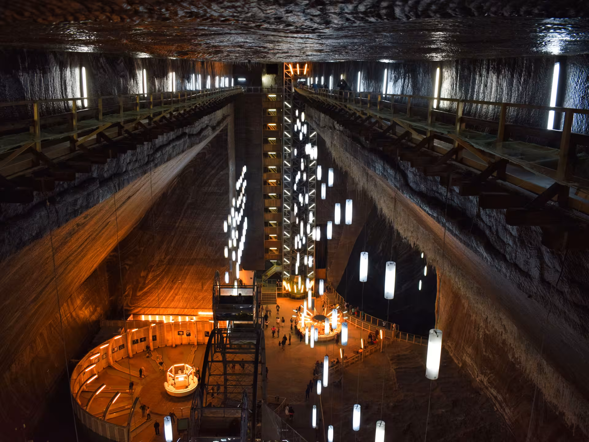 Turda Salt Mine interior with illuminated hanging lights, wooden walkways, and visitors exploring the vast underground cavern