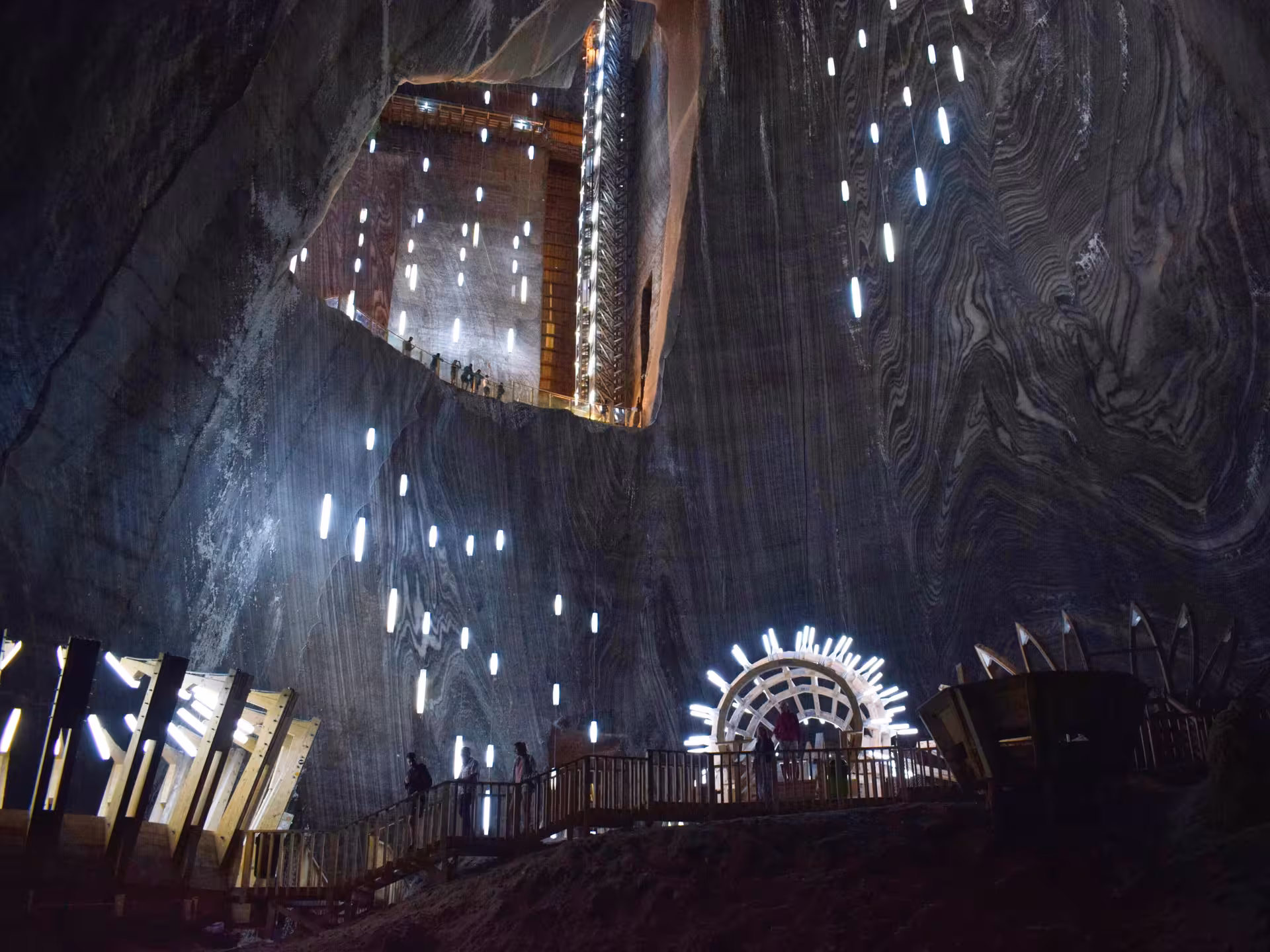 Vast illuminated underground chamber of Turda Salt Mine with visitors exploring on a guided day trip from Cluj