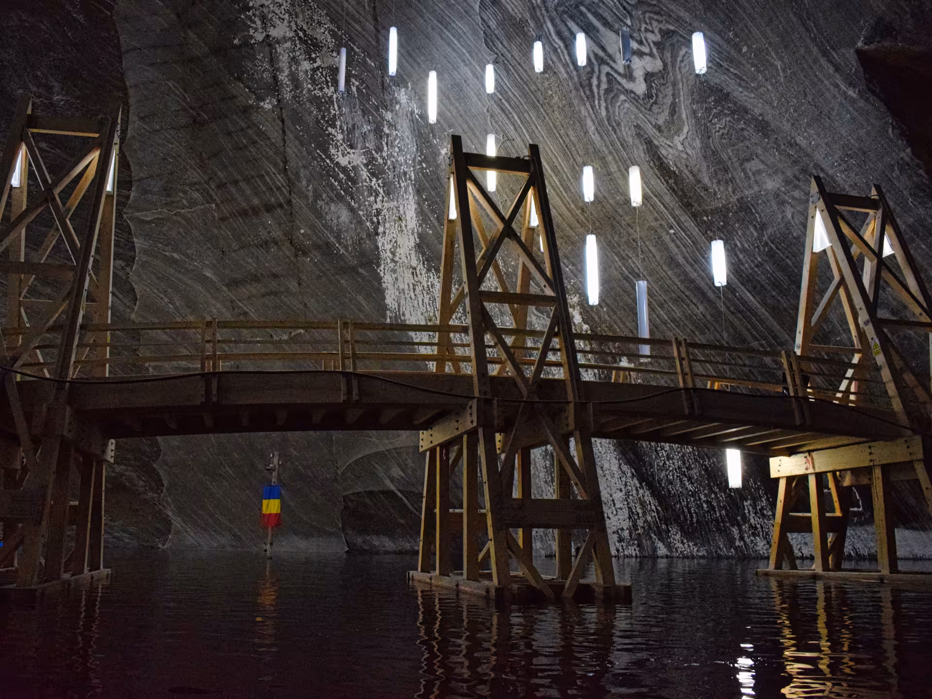 Wooden bridge over underground lake inside Turda Salt Mine with swirling salt walls on a Romania full-day tour