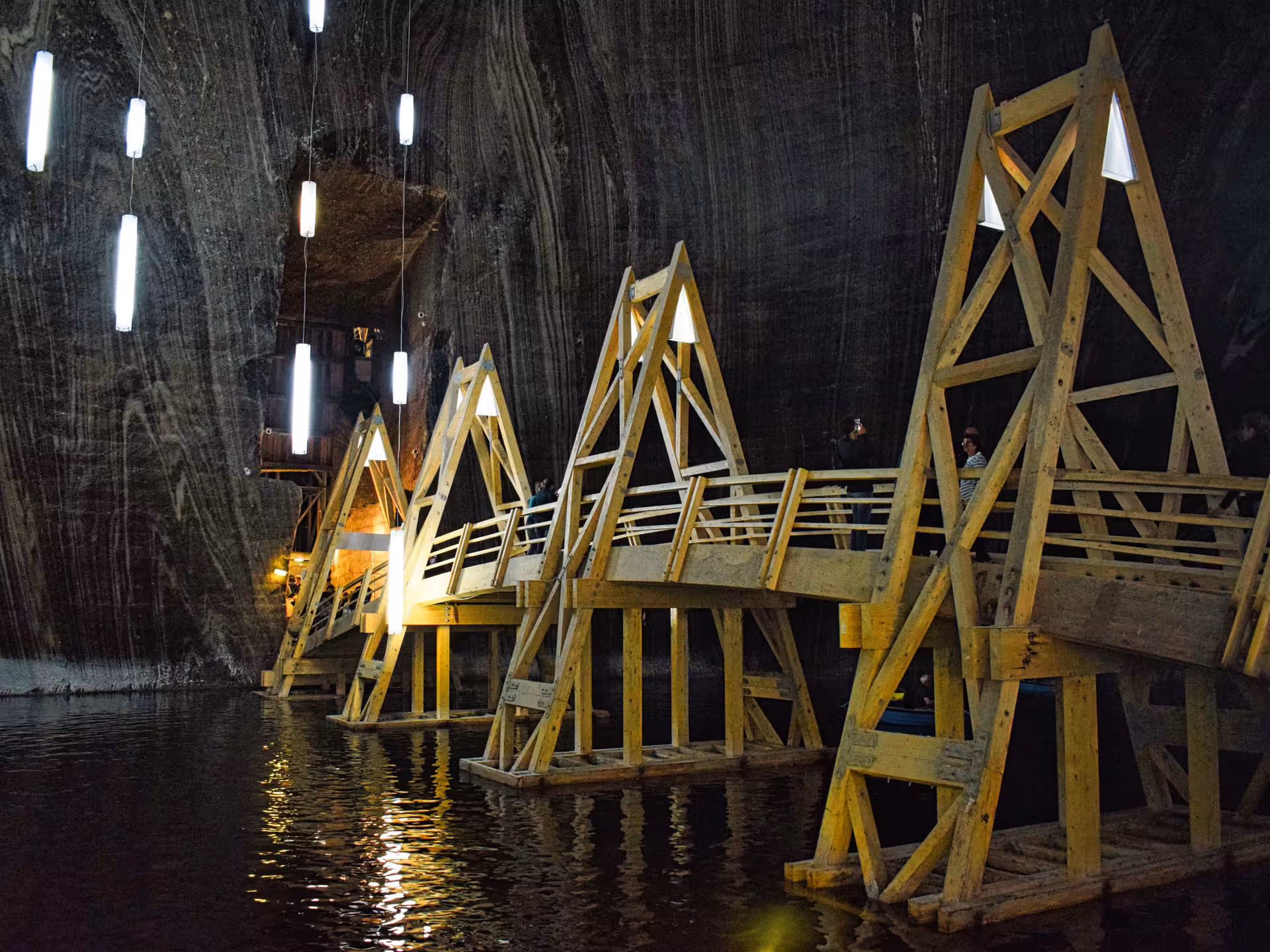 Illuminated wooden walkway over underground lake inside Turda Salt Mine on a day trip from Cluj Romania