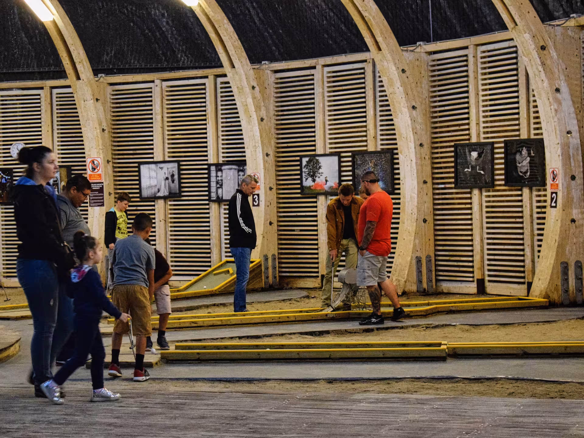 Visitors playing mini golf inside Turda Salt Mine's wooden arched underground hall with sand lanes