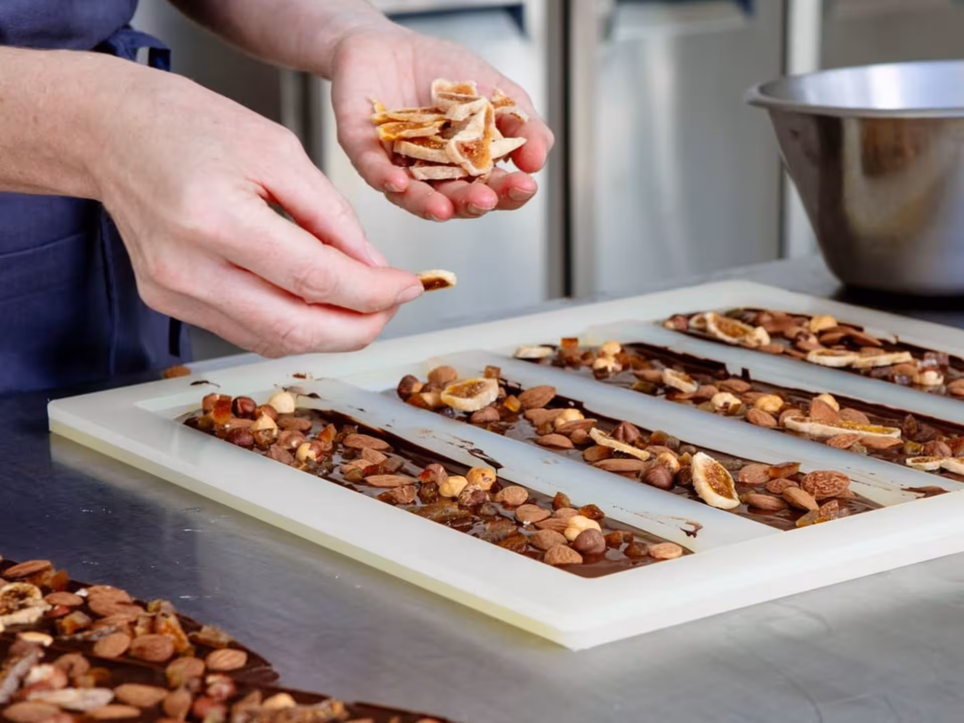 Hands adding dried fruit and nuts to chocolate molds at a Turin Chocolate Factory workshop.