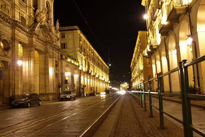 Historic illuminated street in Turin at night with baroque architecture and empty cobblestone road