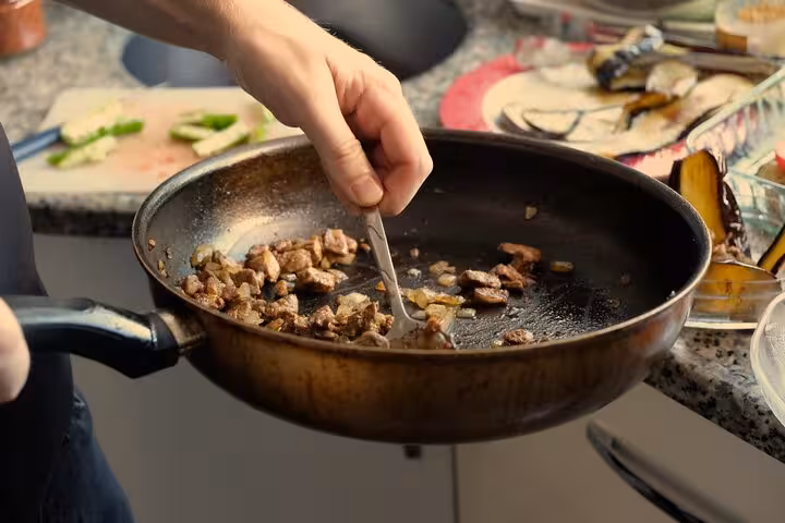 Hands sautéing diced meat in a pan during a private Turkish cooking class with local moms at home