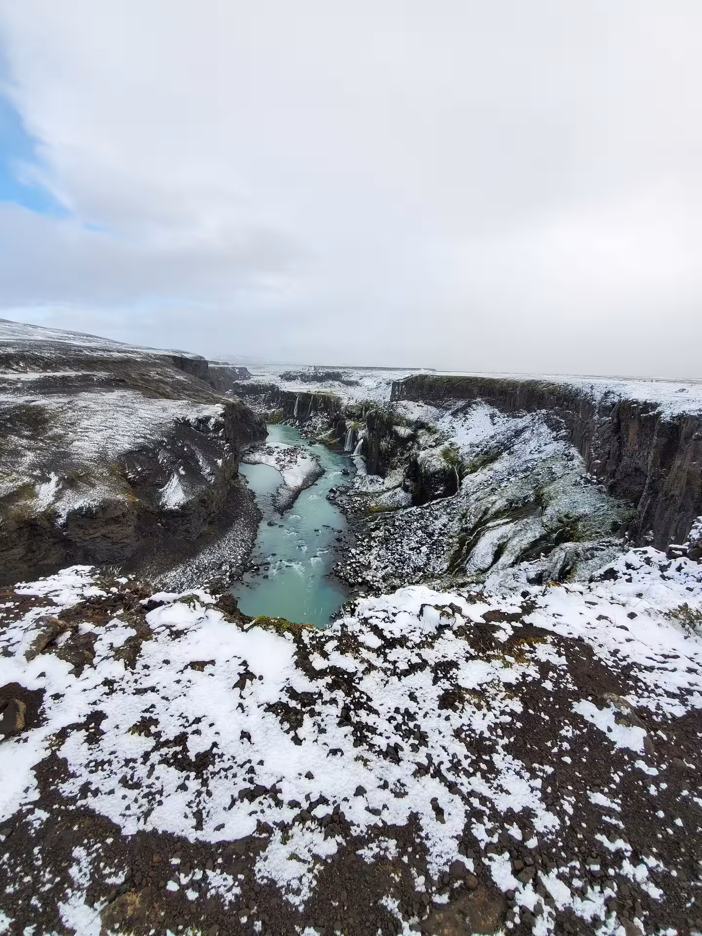 Snow-dusted volcanic rocks surround a turquoise glacial pool at a hidden Iceland waterfall on an exclusive super jeep tour