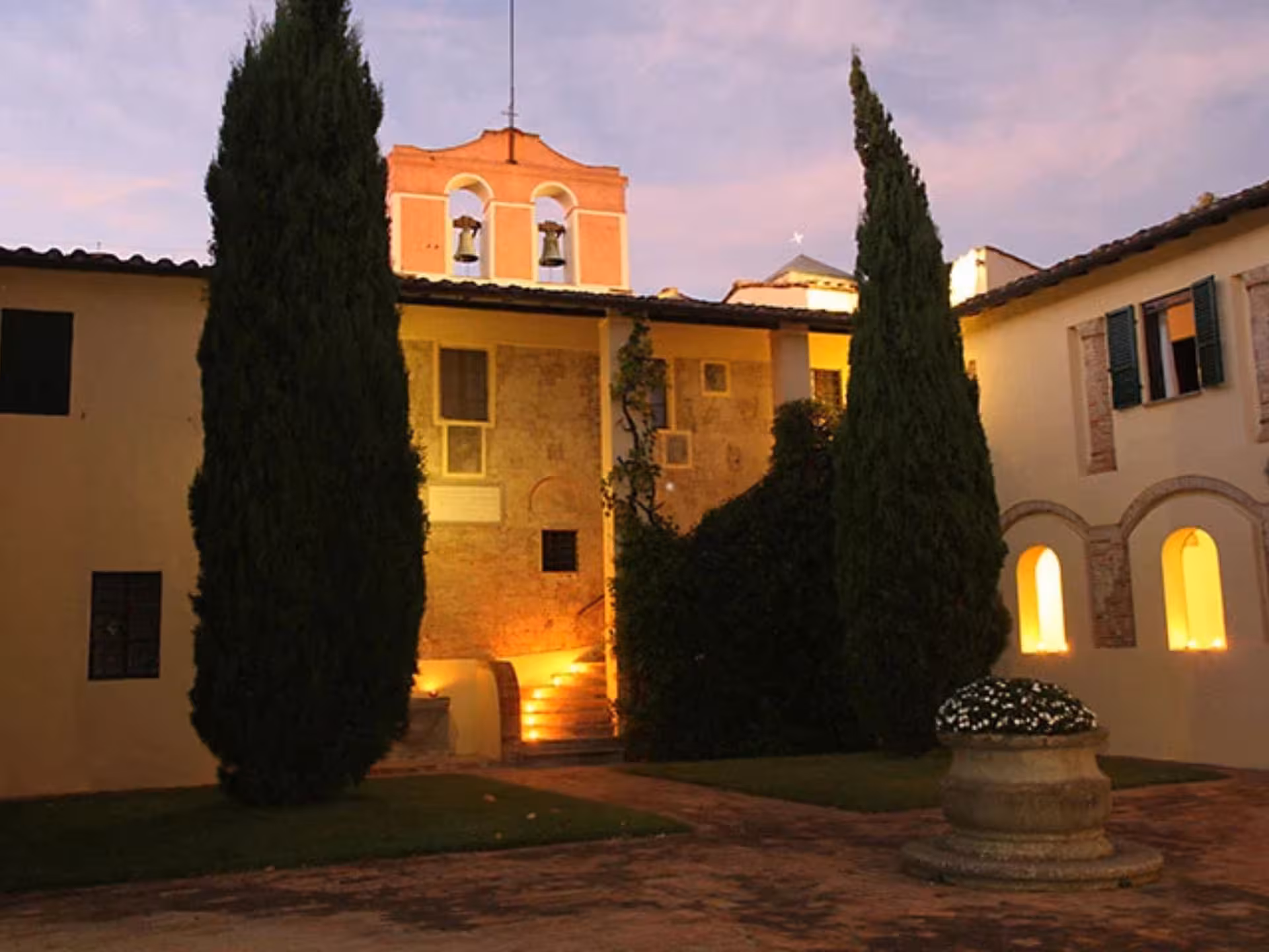 Charming Tuscan abbey illuminated at dusk, perfect for a serene wine tasting and lunch near Pisa.