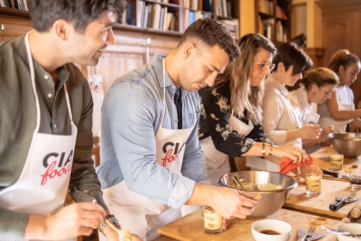 Group enjoying a hands-on Tuscan cooking class, crafting desserts at a rustic table in Florence.