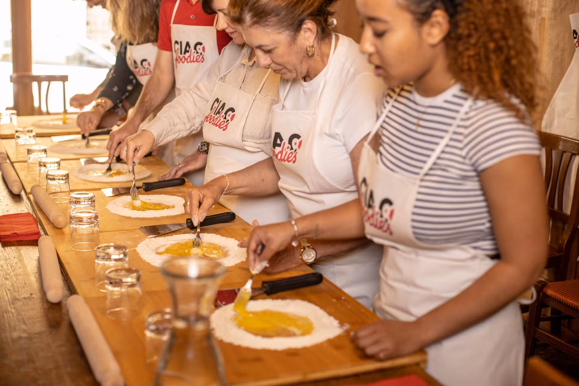 Participants engaged in a Tuscan cooking class, preparing pasta dough on wooden tables in Florence.