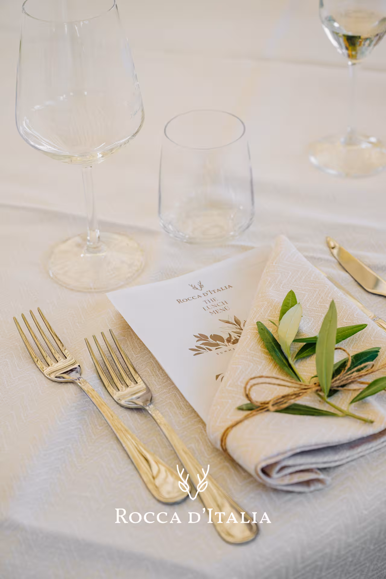 Elegant Tuscan dining setup with a menu, glassware, and olive branch napkin for a luxury supercar tour experience.