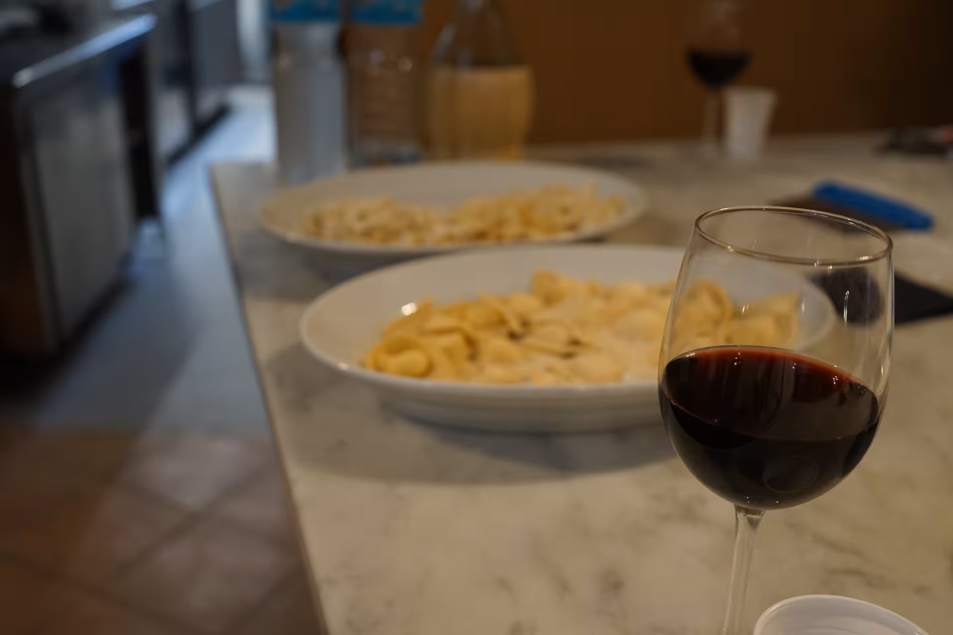 Glass of red wine with plates of fresh pasta on a marble countertop during a Tuscan culinary tour in Florence.