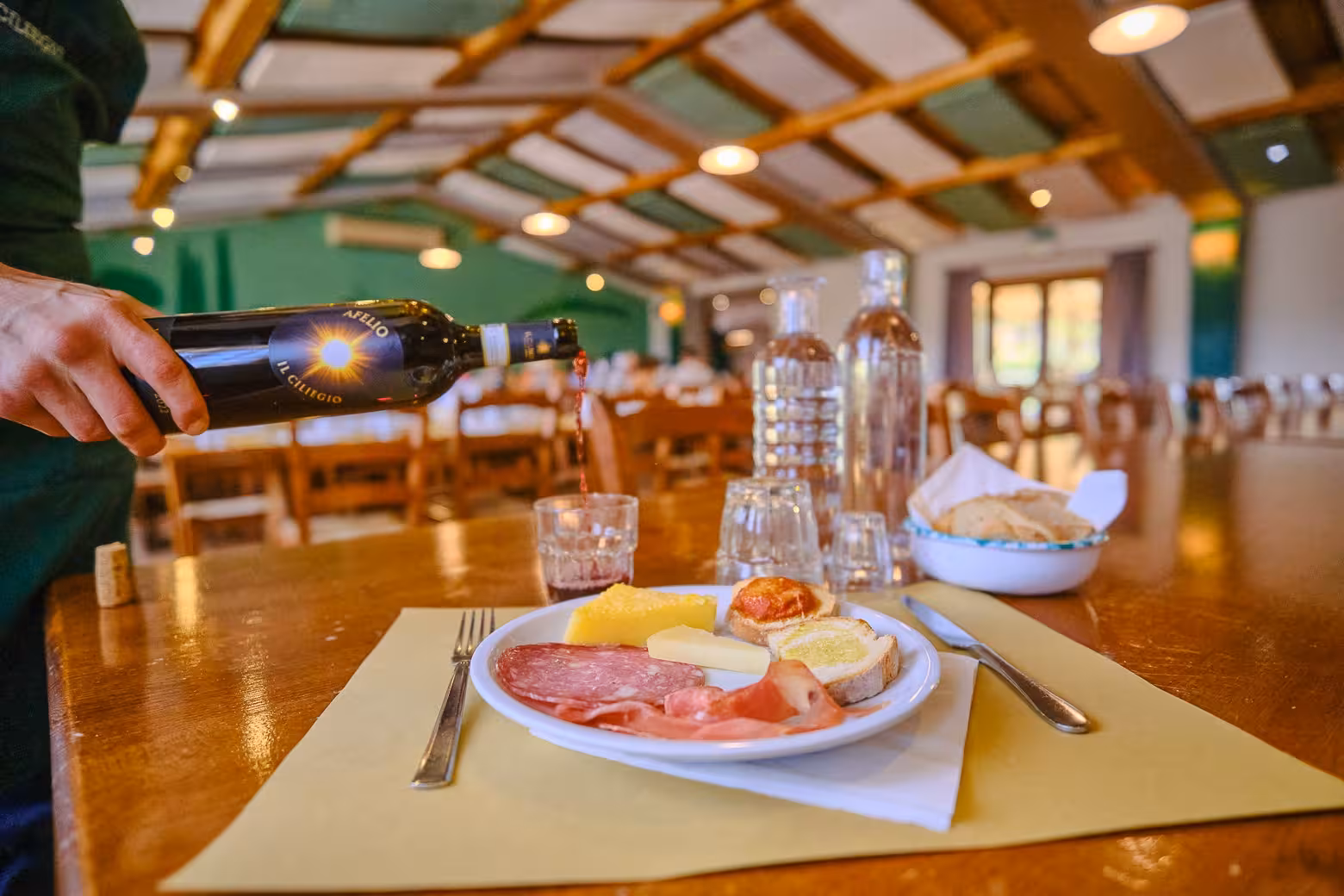 Authentic Italian charcuterie and cheese platter with red wine pouring in a rustic Tuscany restaurant setting.