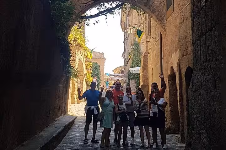 Private Tuscany tour group walking through a medieval stone archway in a historic Tuscan village alley