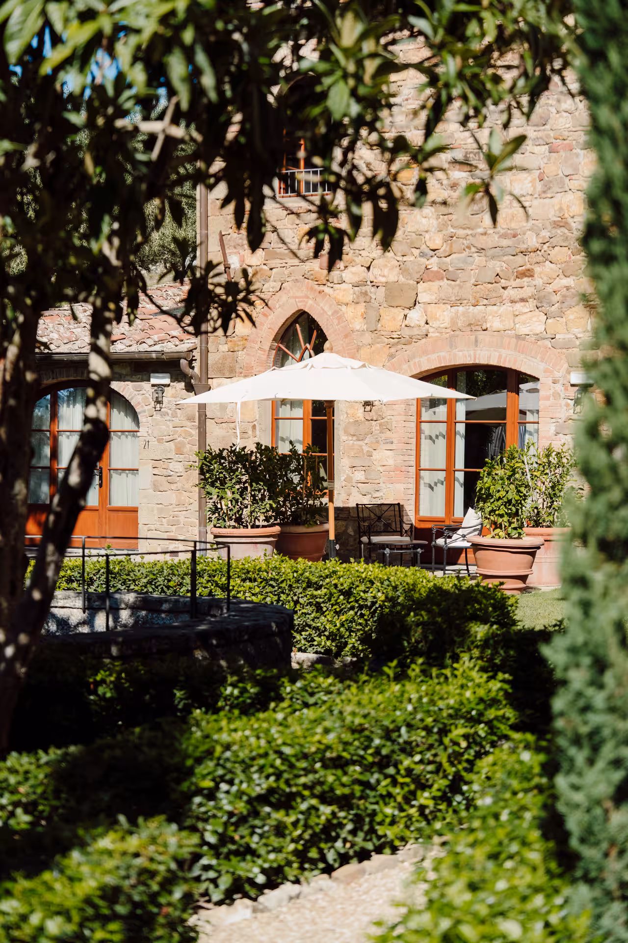 Stone Tuscan villa with white patio umbrella and manicured garden hedges in sunlight