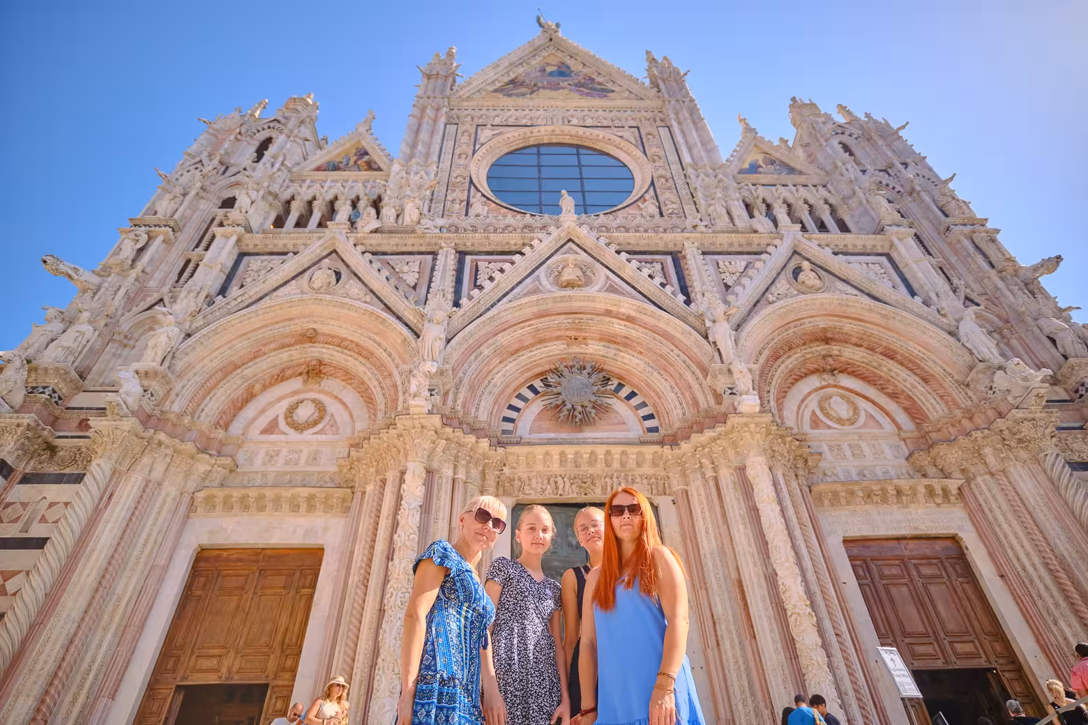Visitors posing in front of the stunning Gothic facade of Siena Cathedral on a Tuscany guided tour.